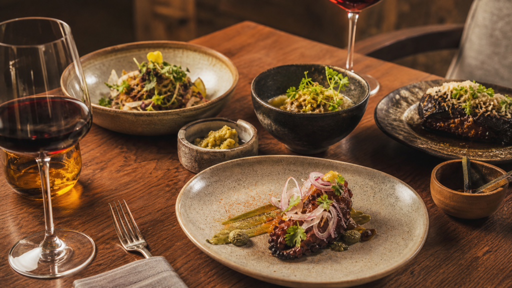 Platillos mexicanos contemporáneos y copas de vino en una mesa de experiencia gastronómica.