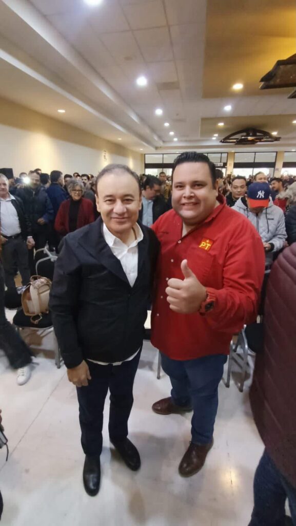 Dos asistentes posan durante un encuentro político en Hermosillo; uno viste una camisa roja con el emblema del PT